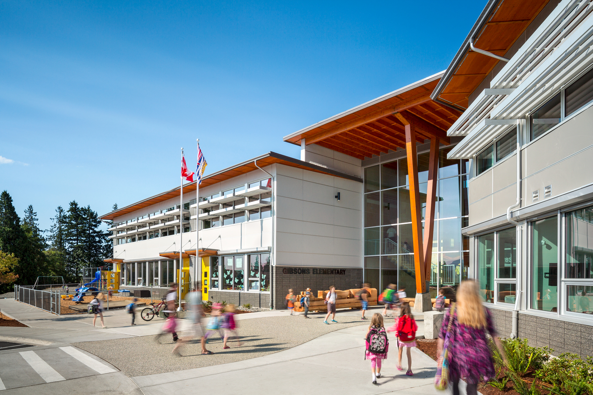 Glue-laminated timber beams and columns support the cantilever roof overhang in this exterior view of Gibsons Elementary School as children enter on a sunny day