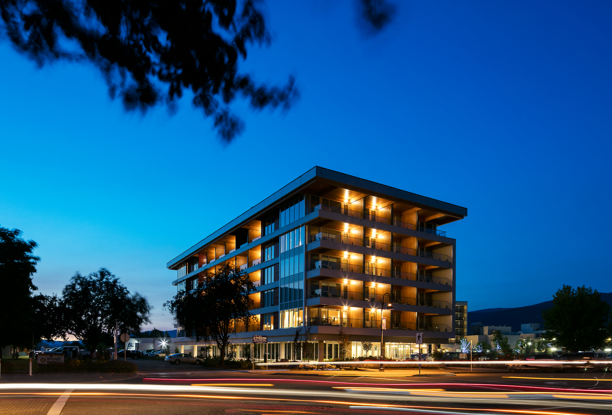 Exterior evening across the street view of The West Wing, Penticton Lakeside Resort and Conference Centre mid rise, showing warmly lit balconies with blue evening sky in background