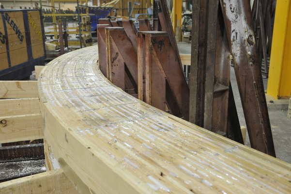 Close up interior image of curved glue-laminated timber (glulam) beam in factory during construction process.